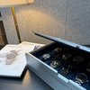 AUBLIQ silver watch box with its lid partly closed, revealing watches on blue cushions beside watch magazines.