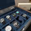 Close-up of the AUBLIQ silver watch box interior with assorted watches, blue-lined slots and a removed watch cushion.