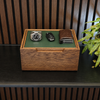 A rectangular wooden storage box with a green interior tray sits on a dark tabletop. Inside the box are a silver wristwatch, a black car key fob, and a brown leather wallet.