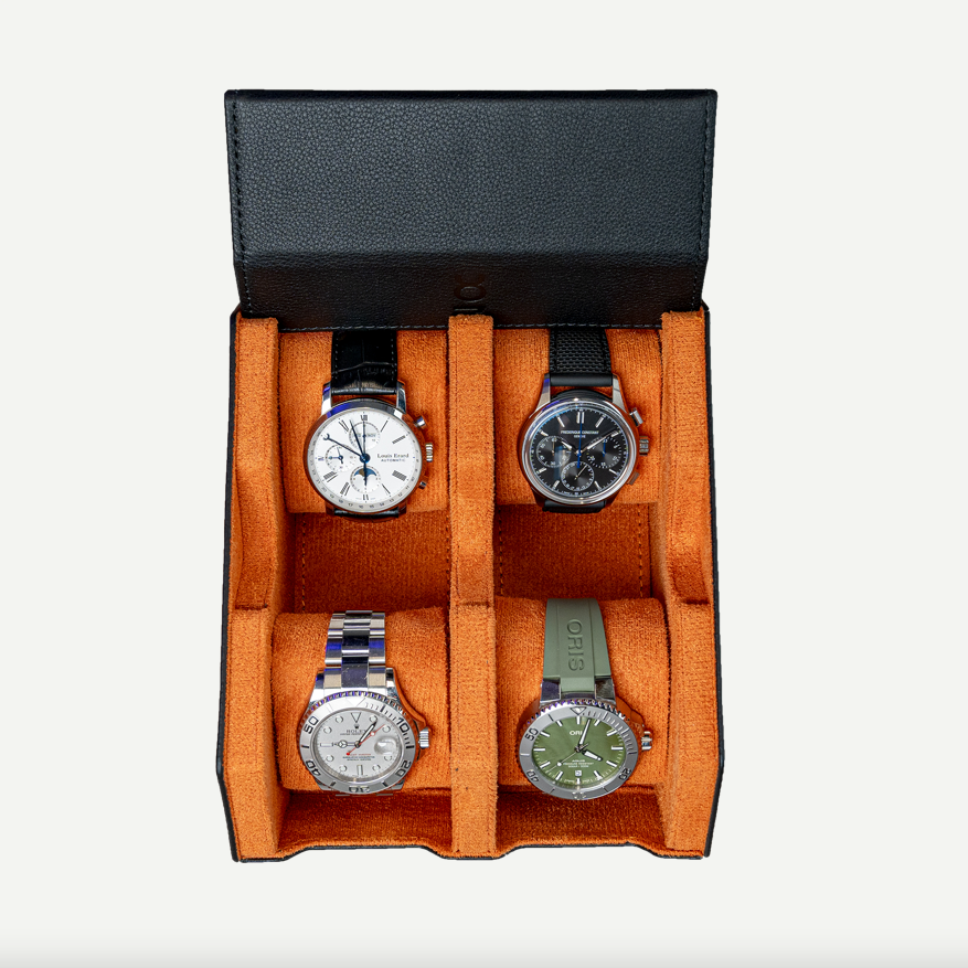 A black leather watch box open, displaying four watches with orange cushions.