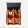 A black leather watch box open, displaying four watches with orange cushions.